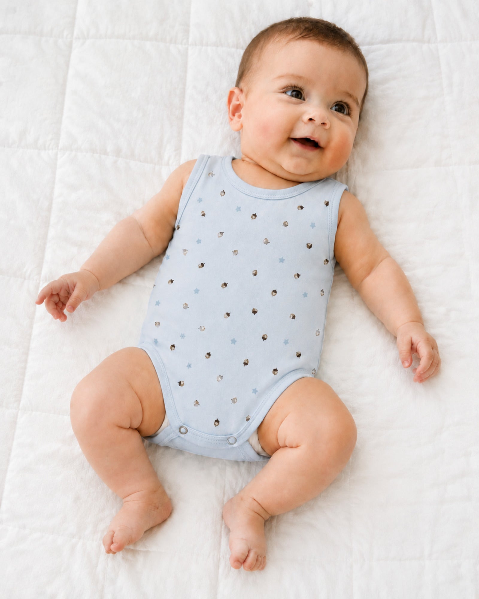 Baby wearing sky blue acorn and star print sleeveless bodysuit in a bright natural use-case setting