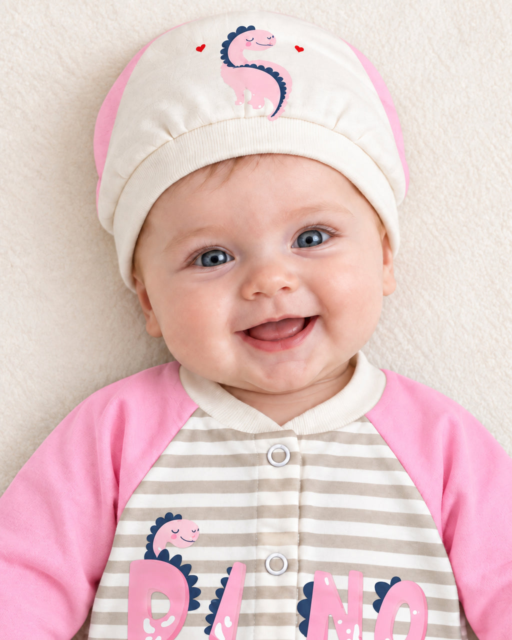 Baby Dream pink dinosaur sleepsuit and hat set, close baby portrait with matching dinosaur cap
