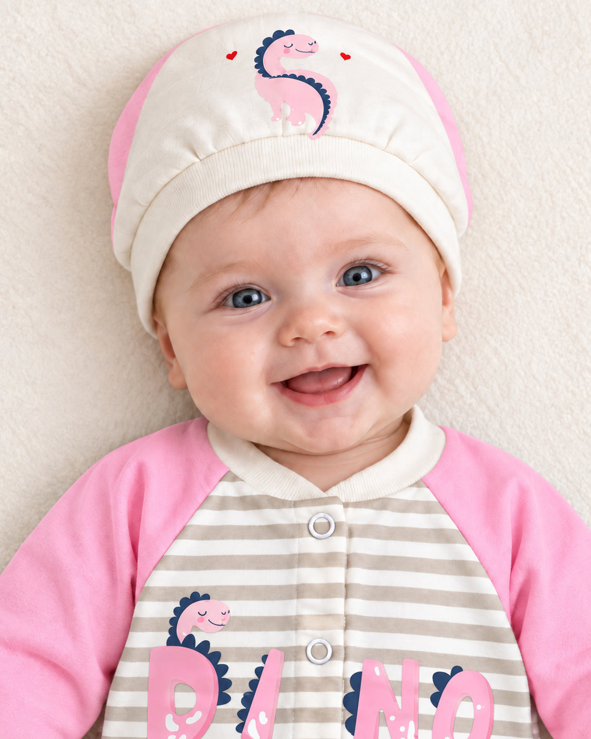 Baby Dream pink dinosaur sleepsuit and hat set, close baby portrait with matching dinosaur cap