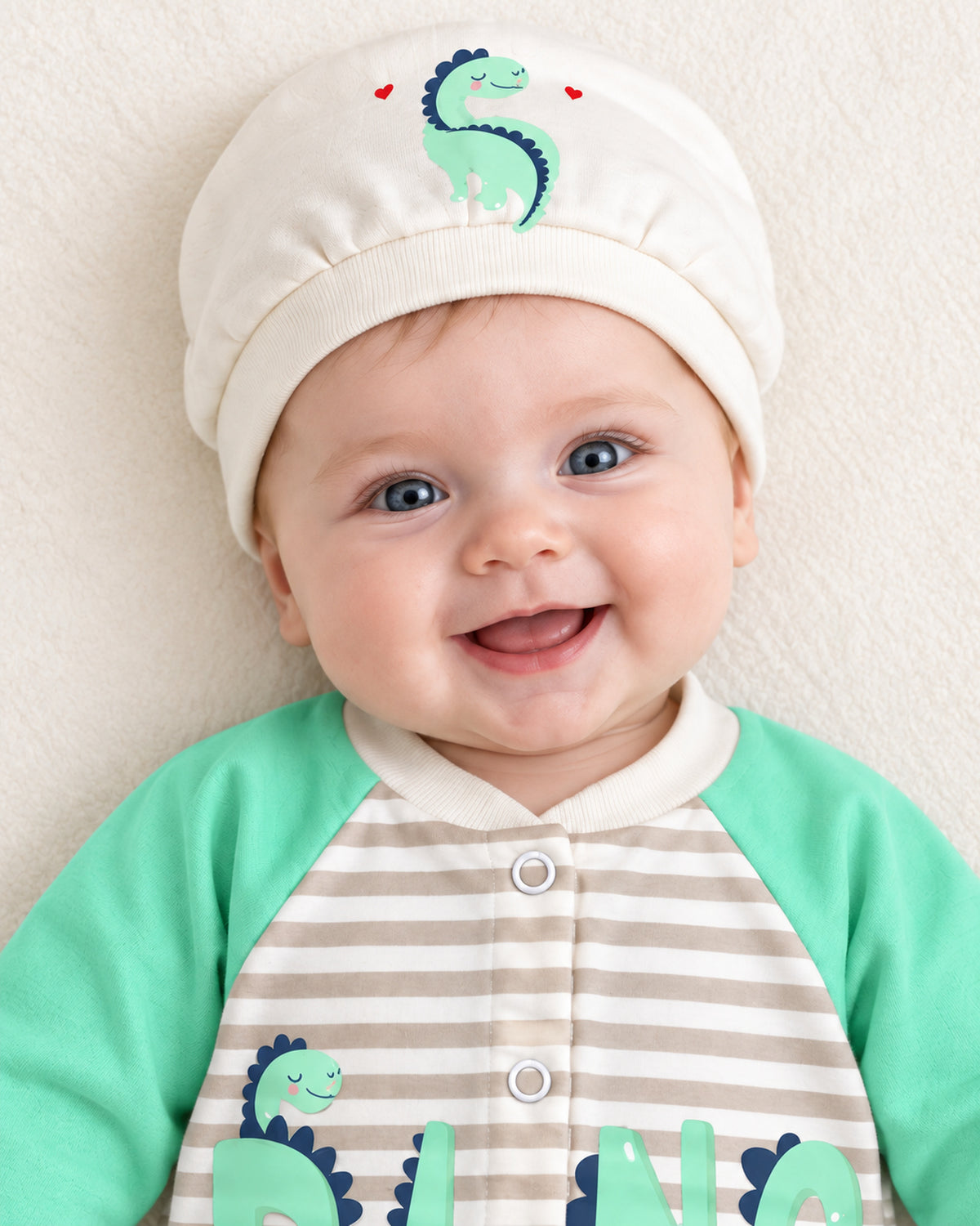 Baby Dream pistachio dinosaur sleepsuit and hat set, close baby portrait with matching dinosaur cap