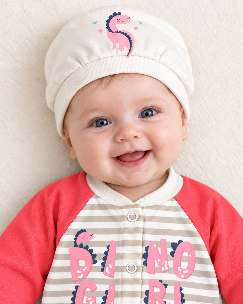 Baby Dream neon red dinosaur sleepsuit and hat set, close baby portrait with matching dinosaur cap